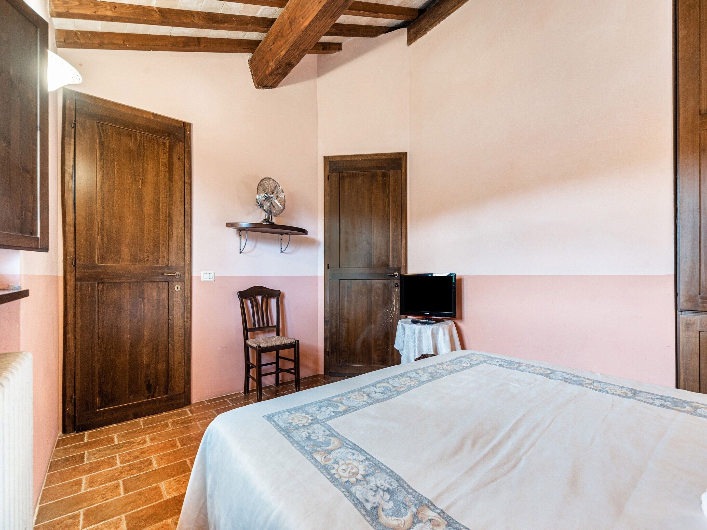 A bedroom with a bed, a chair, a TV on a small table, and wooden doors.