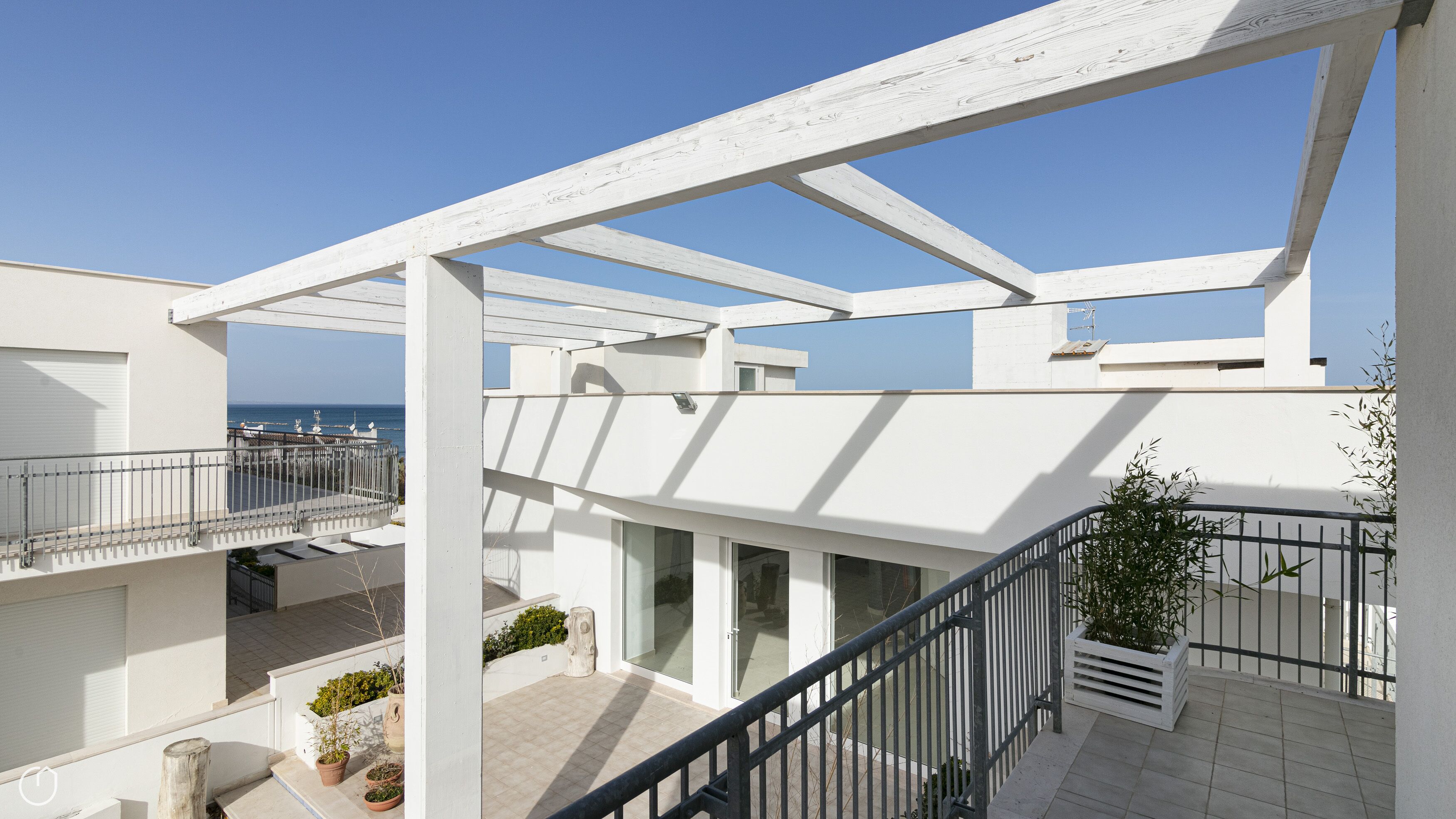 A multi-level residential building with balconies, a view of the sea, and potted plants.