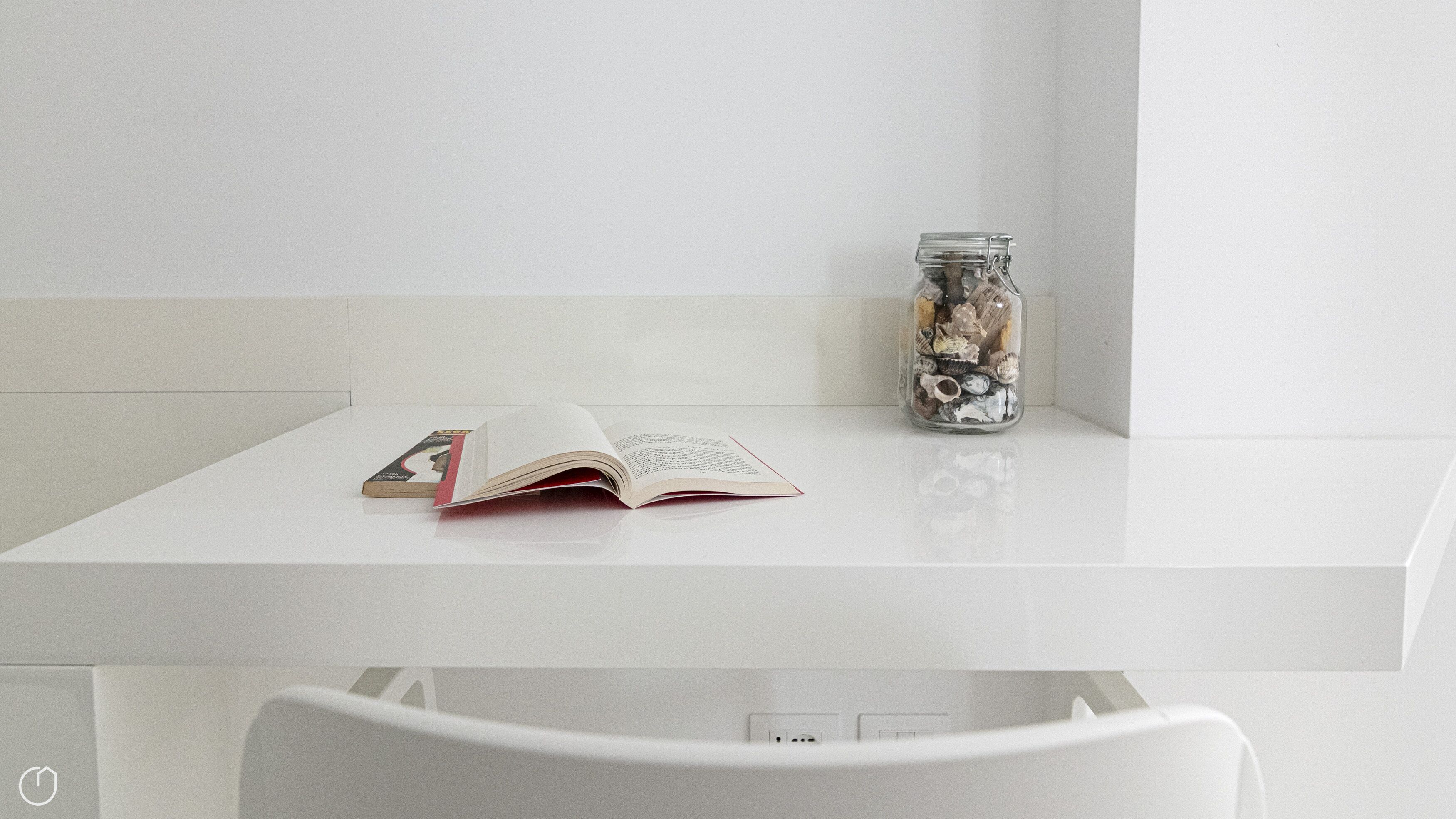 A white table with a book and a jar of seashells.