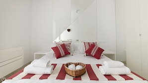 A modern hotel room with a large bed, white bedding, red and white striped towels, and a wicker basket with towels. - Rivazzurra Homes - 55 (Termoli)