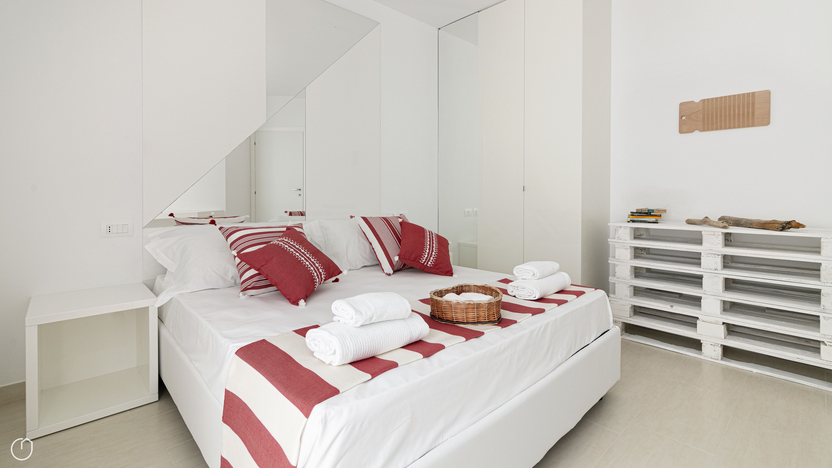 A modern bedroom with a bed, pillows, a bedside table, a wall-mounted shelf, and a wooden shelf unit.