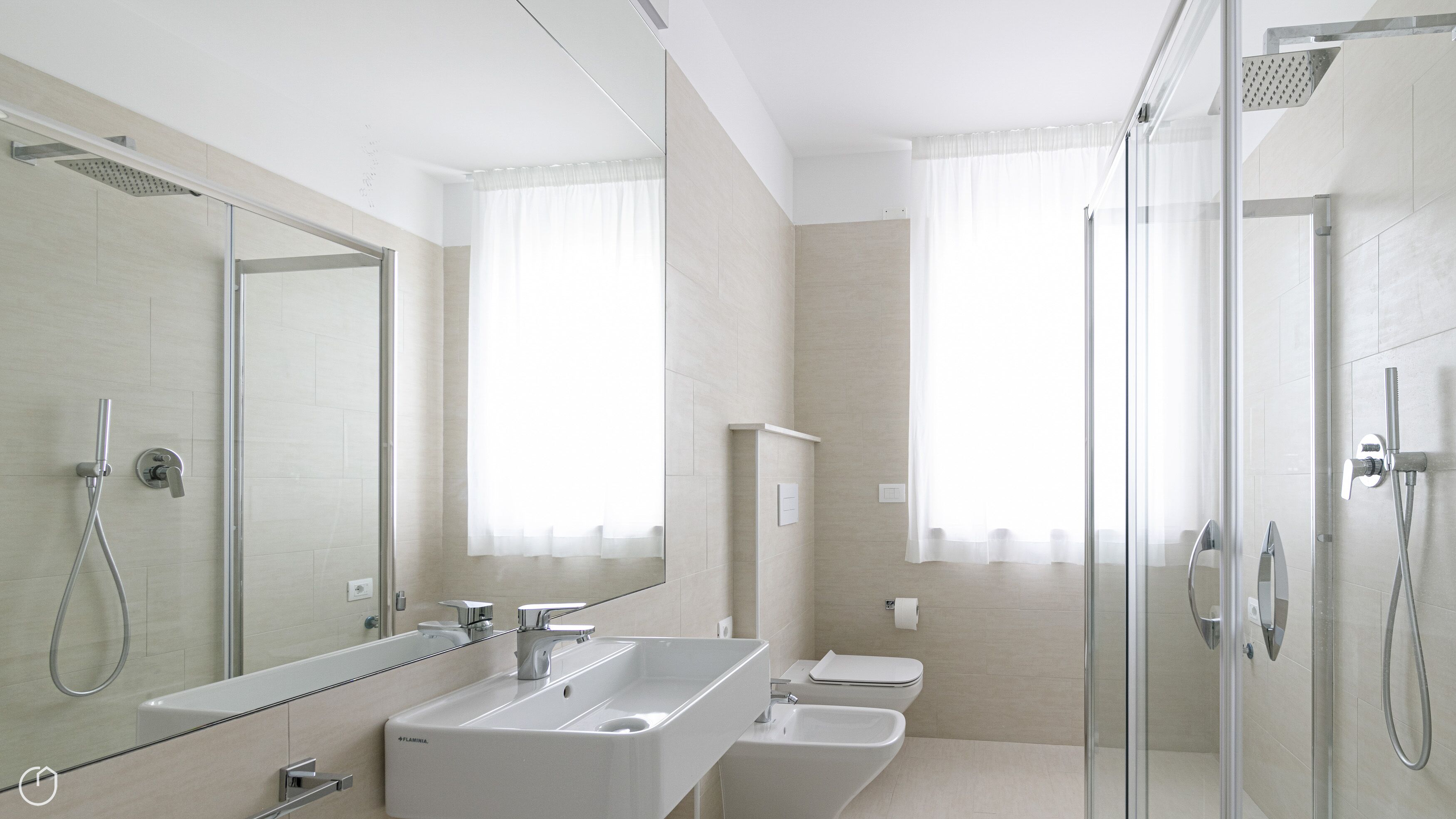 A modern bathroom with a large mirror, a double sink, a shower, and a toilet.