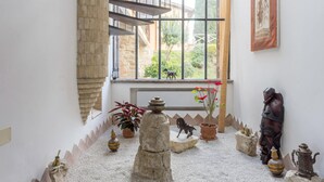 Una stanza con parete in pietra, una finestra vista giardino e diversi oggetti decorativi, tra cui un vaso con fiori, una statua e un servizio da tè tradizionale.