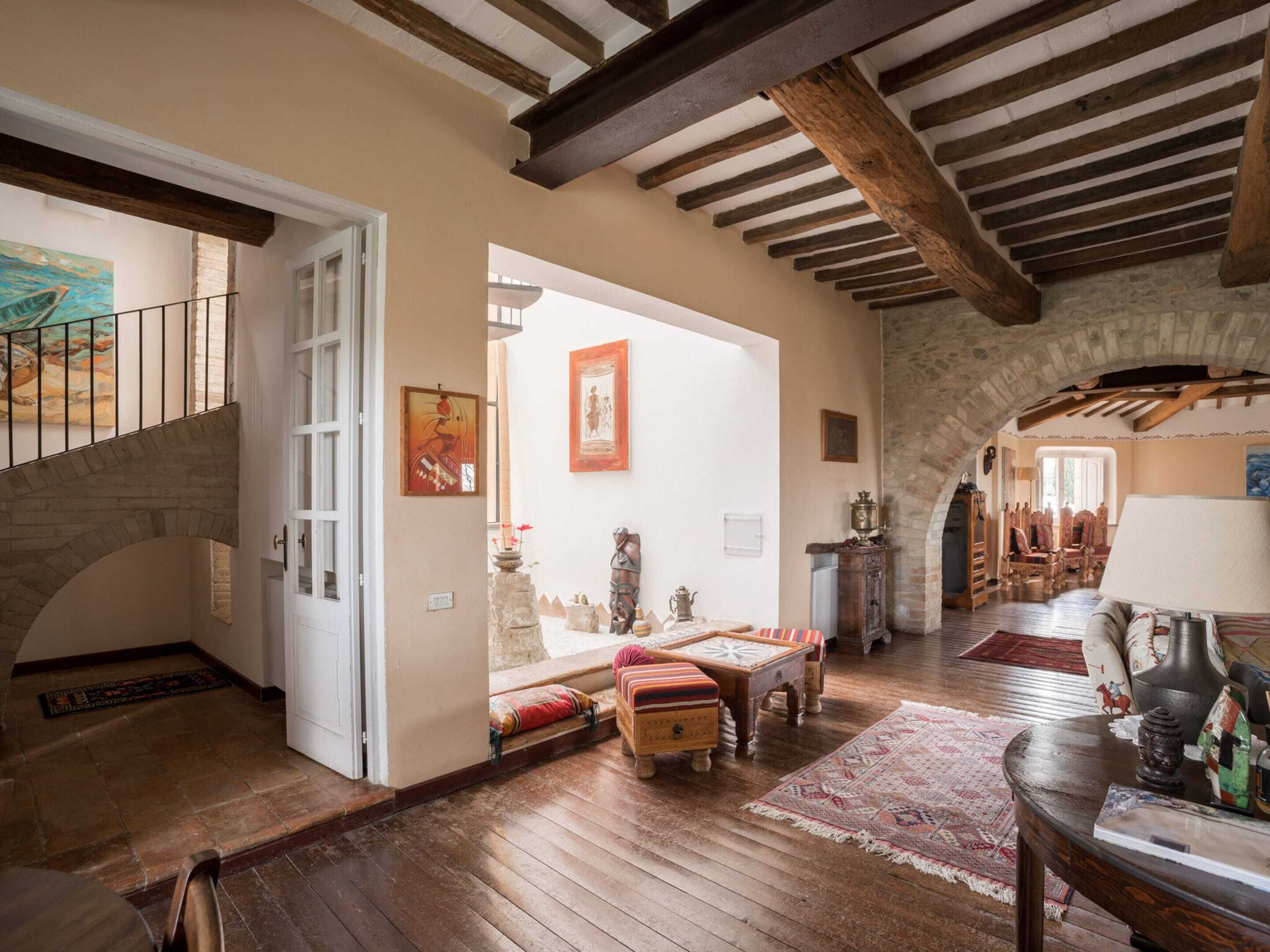 A spacious living area with a wooden staircase, rustic stone walls, and a cozy seating area with a patterned rug.