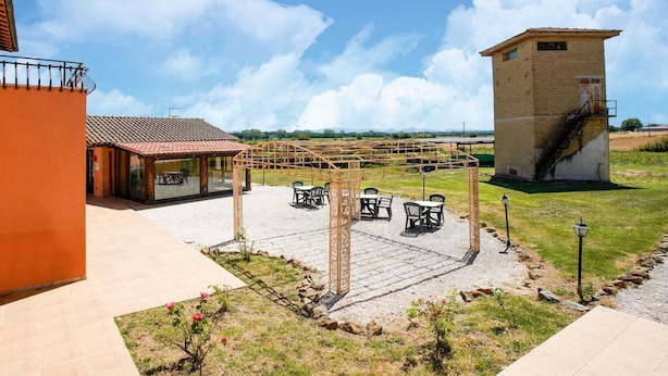 Un patio con mesas al aire libre, un edificio con techo de tejas y una estructura de torre.