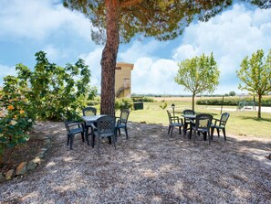 An outdoor seating area with tables and chairs, surrounded by gravel and trees, with a building in the background. - Apartment in Castiglione Near Lake Trasimeno (Castiglione del Lago)