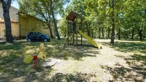 A playground with a slide and climbing structure, surrounded by trees and a parked car. - Holiday Home Near Castiglione del Lago (Castiglione del Lago)