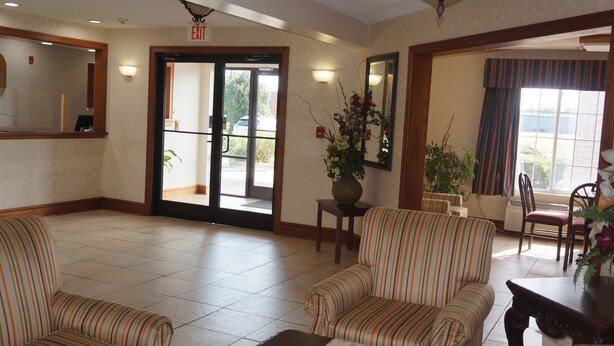 A lobby with striped chairs, a large vase with flowers, and a door leading outside. - Scotland Neck Inn (Scotland Neck)