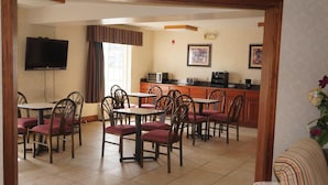A dining area with multiple tables and chairs, a television mounted on the wall, and a kitchen area with appliances. - Scotland Neck Inn (Scotland Neck)