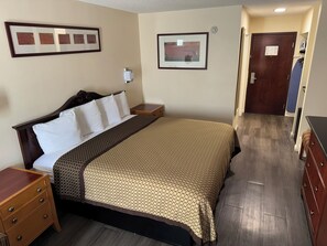 A hotel room with a large bed, a bedside table, a wardrobe, and a door leading to another room. - Scotland Neck Inn (Scotland Neck)