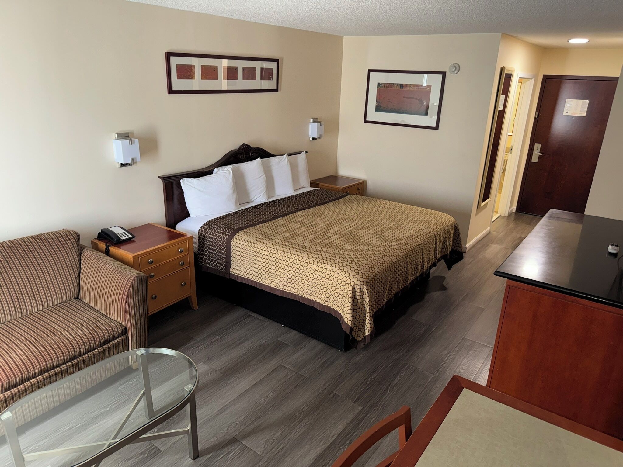 A hotel room with a bed, a chair, a desk, and a glass table.