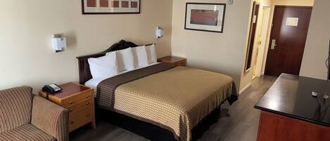 A hotel room with a bed, bedside tables, a desk, a chair, and a small table.