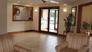 A lobby with striped chairs, a reception desk, and a glass door leading outside. - Scotland Neck Inn (Scotland Neck)