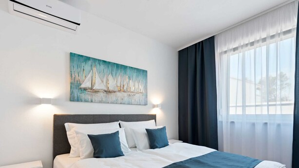 A hotel room with a bed, a painting of sailboats, a window with curtains, and an air conditioning unit. - Holiday Home in Vir Near sea Beach (Vir)