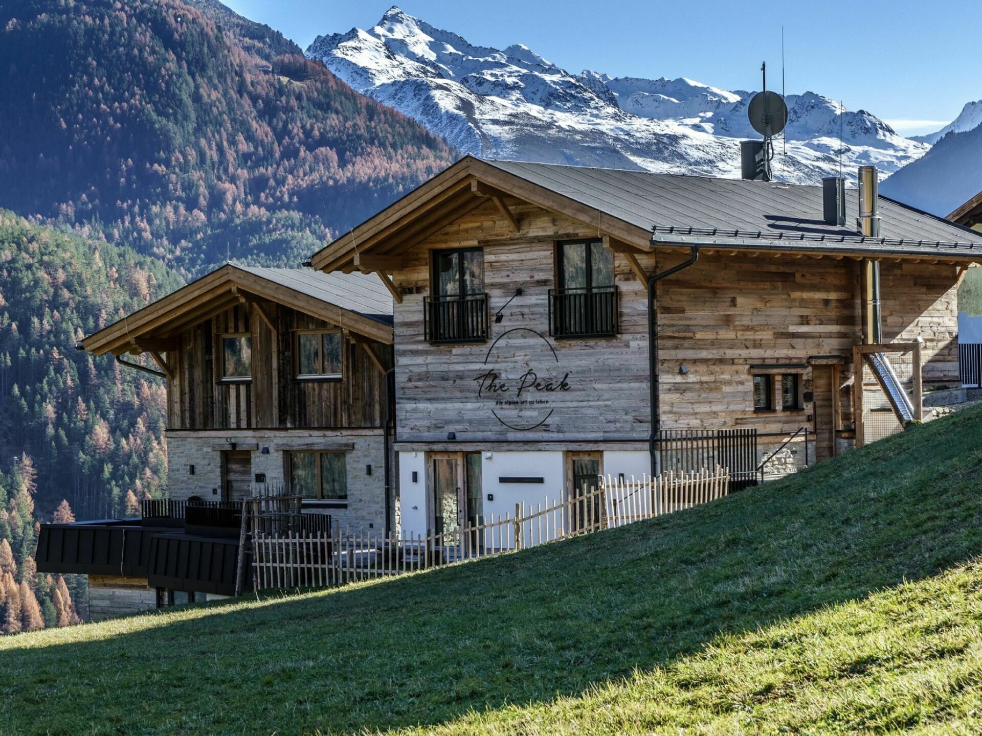 A wooden chalet with a sign reading "The Peak" and a view of snow-capped mountains in the background.