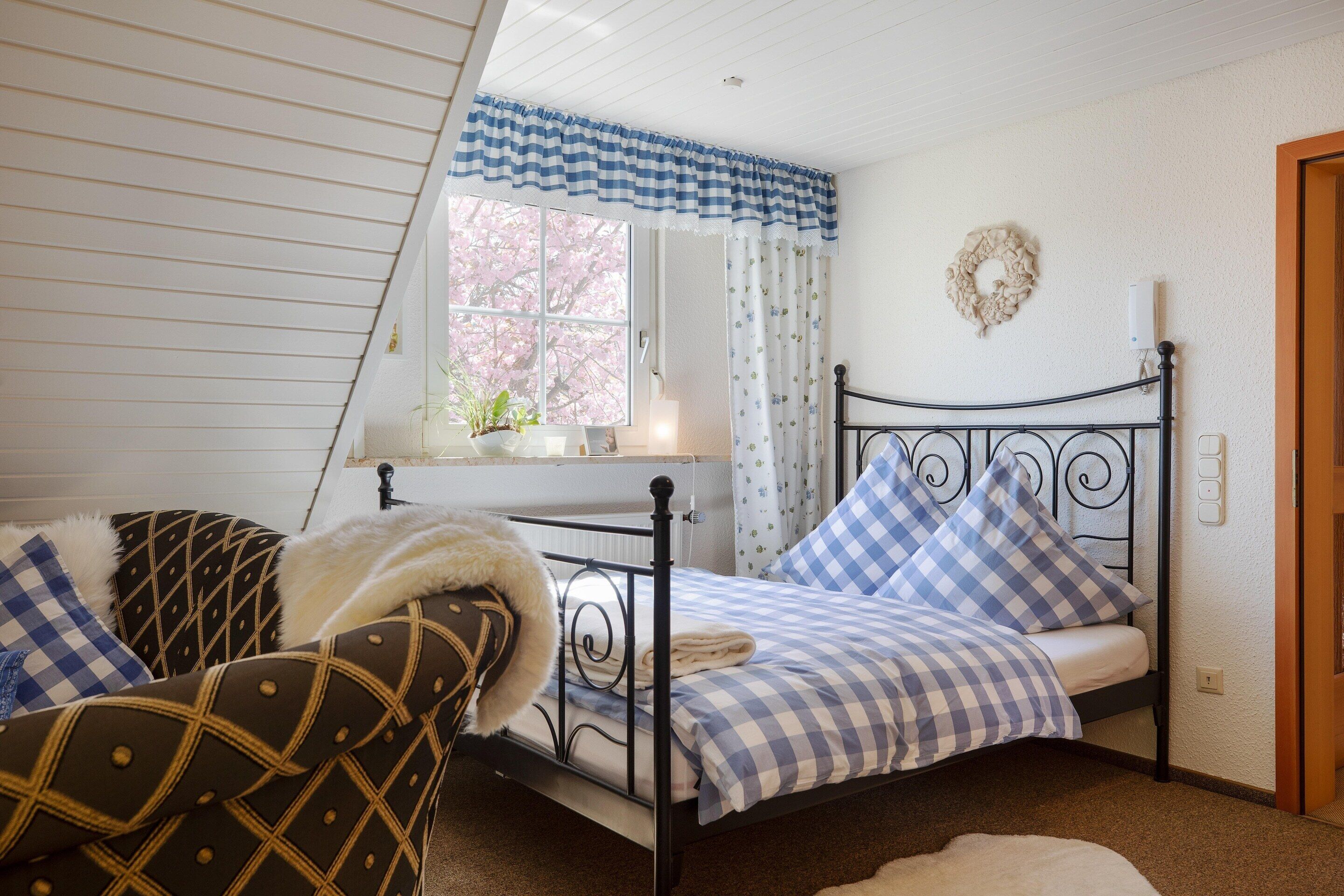 A bedroom with a bed, a window with curtains, a wall decoration, and a bedside table.