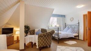 A cozy bedroom with a sloped ceiling, a bed with checkered bedding, a chair with a patterned cushion, a television on a wooden stand, and a small table with a lamp. - Ferienwohnung in Oberfranken mit Garten (Weissenbrunn)