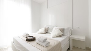 A modern, minimalist bedroom with a neatly made bed, a bedside table, and a wicker basket with towels. - Rivazzurra Homes - 56 (Termoli)