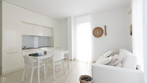 A modern, minimalist living space with a kitchen, dining area, and a white sofa. - Rivazzurra Homes - 56 (Termoli)
