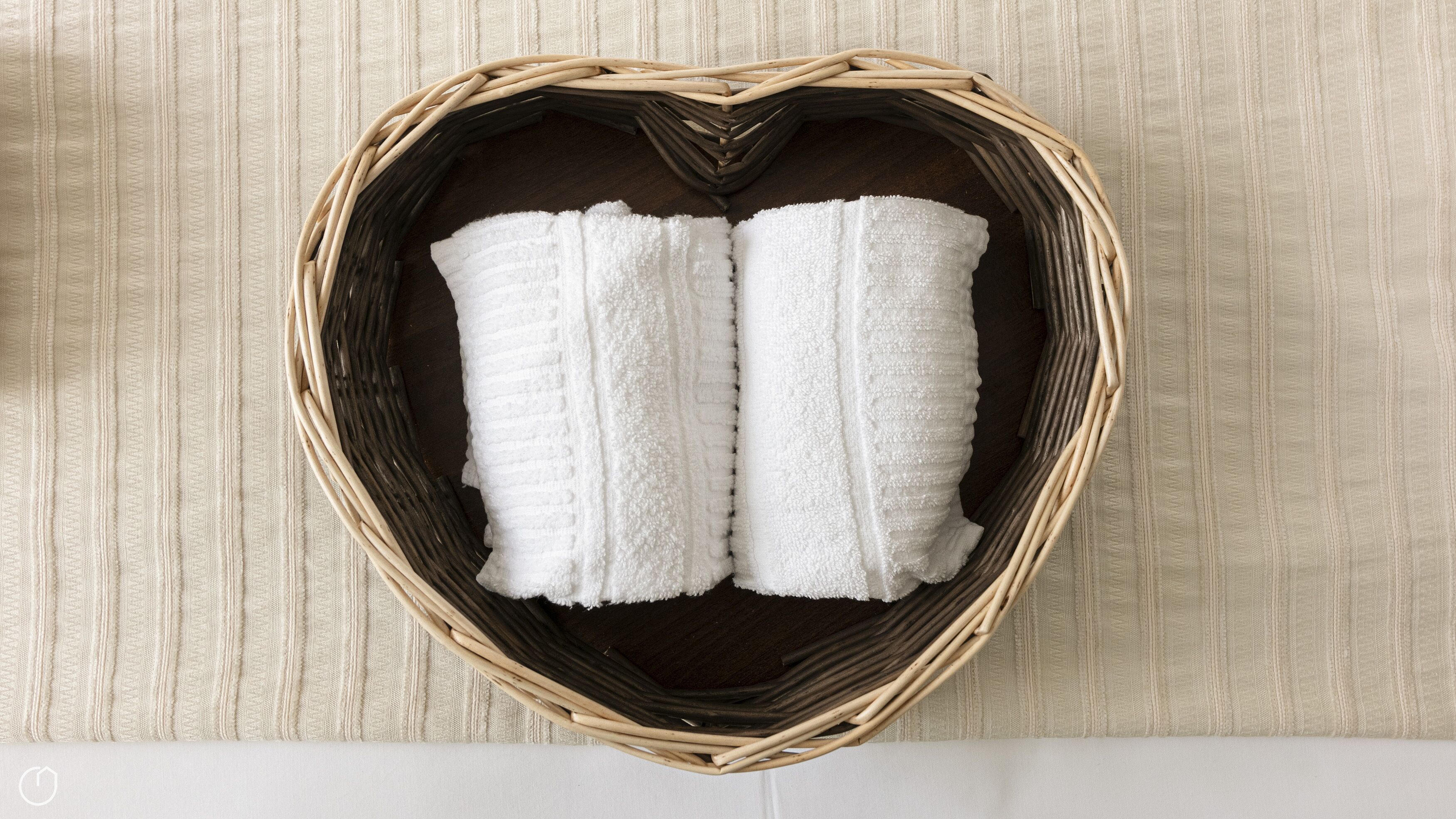 A heart-shaped wicker basket containing two white towels on a wooden floor.