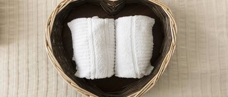 A heart-shaped wicker basket containing two white towels on a wooden floor.