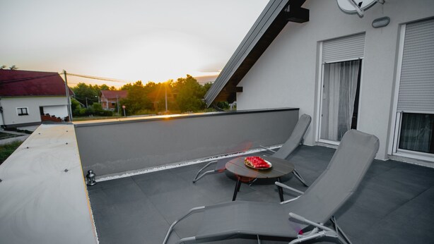 Een terras op het dak met twee loungestoelen en een tafeltje, met uitzicht op een zonsondergang.