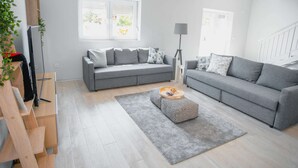 Een moderne woonkamer met twee grijze banken, een houten dressoir en een vloerlamp.