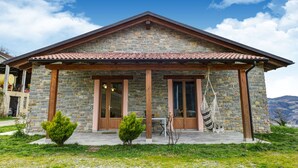 A stone house with a tiled roof, wooden doors, and a small porch area.