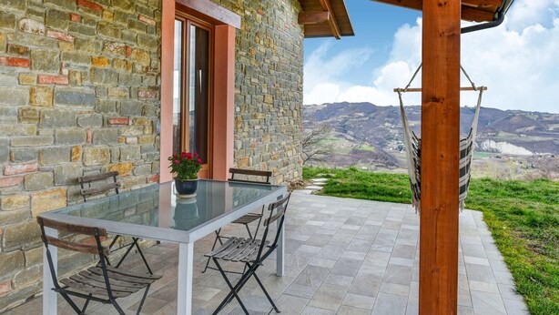 A stone building with a wooden pergola, a glass table with chairs, and a hammock.