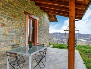 Un bâtiment en pierre avec une pergola en bois, une table en verre avec des chaises et un hamac.