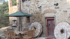 Un bâtiment rustique en pierre, avec une table et des chaises en bois, une porte rouge et de grandes roues en pierre.
