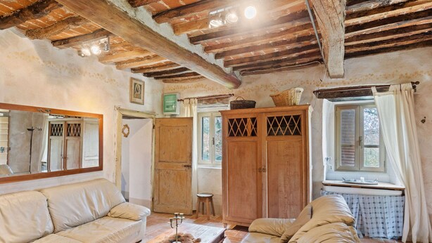 Un salon rustique avec des poutres apparentes, un grand miroir, un canapé, un meuble en bois et une fenêtre avec des rideaux.