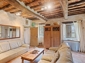 A rustic living room with exposed wooden beams, a large mirror, a sofa, a wooden cabinet, and a window with curtains. - Tuscan Country House Near Castiglion Fiorentino (Castiglion Fiorentino)