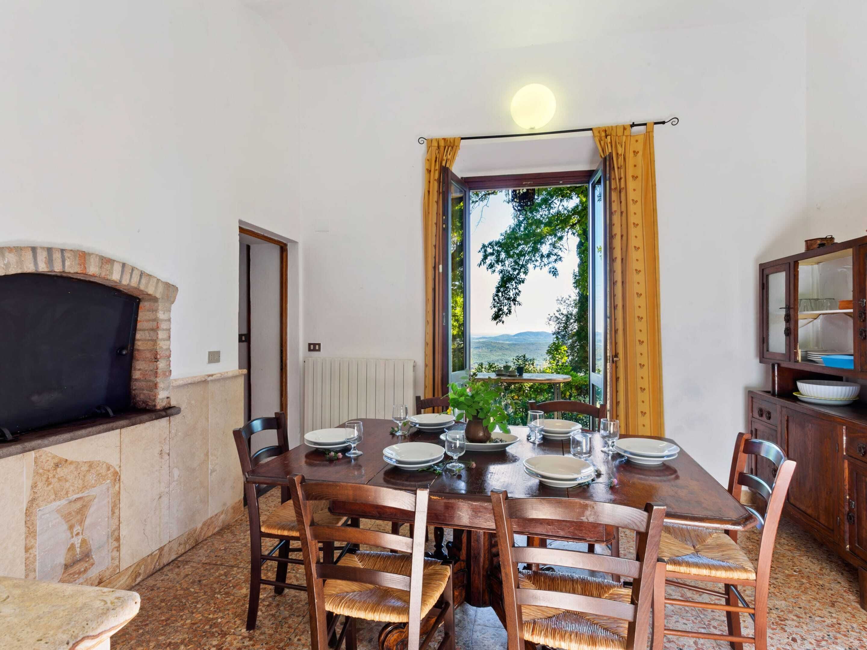 Comedor con chimenea de ladrillo, una mesa dispuesta para seis personas y vistas a través de un ventanal grande.