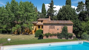 A swimming pool with a tiled deck, surrounded by a well-maintained lawn and a brick building with arched windows.