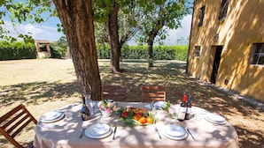 An outdoor dining table set up in a garden with a tablecloth, chairs, and a bottle of wine.
