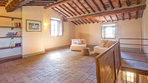 A spacious loft with exposed wooden beams, a brick floor, and a cozy seating area with a sofa and armchairs.