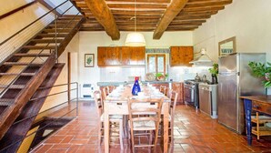 A rustic kitchen with wooden beams, a dining area with a long table, and a staircase.