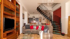Ein Wohnzimmer mit einer Couch, Fernseher, Holzregalen und einer Treppe.