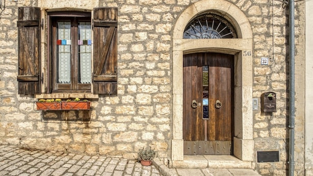 Ein Steinhaus mit Holztür und -fenster, einem Briefkasten und einem Blumentopf.