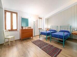 Une chambre avec deux lits, une commode en bois, une chaise et un tapis à motifs.
