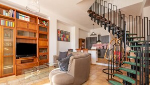Ein geräumiges Wohnzimmer mit moderner Treppe, einer gemütlichen Couch und einer gut sortierten Bücherwand.