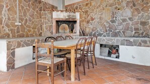 A stone-walled outdoor dining area with a brick fireplace, wooden chairs, and a tiled floor. - Apartment in Agropoli With Garden (Agropoli)