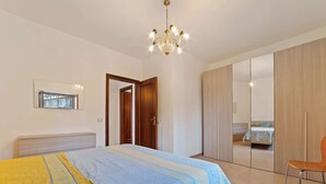 A bedroom with a bed, a chair, a wardrobe, and a mirror. - Apartment in Agropoli With Garden (Agropoli)