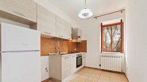 A modern kitchen with white cabinets, a built-in oven, and a window with a view of trees. - Apartment in Agropoli With Garden (Agropoli)