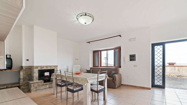 A spacious dining area with a stone fireplace, a dining table with chairs, and a view of the outside through a window. - Apartment in Agropoli With Garden (Agropoli)