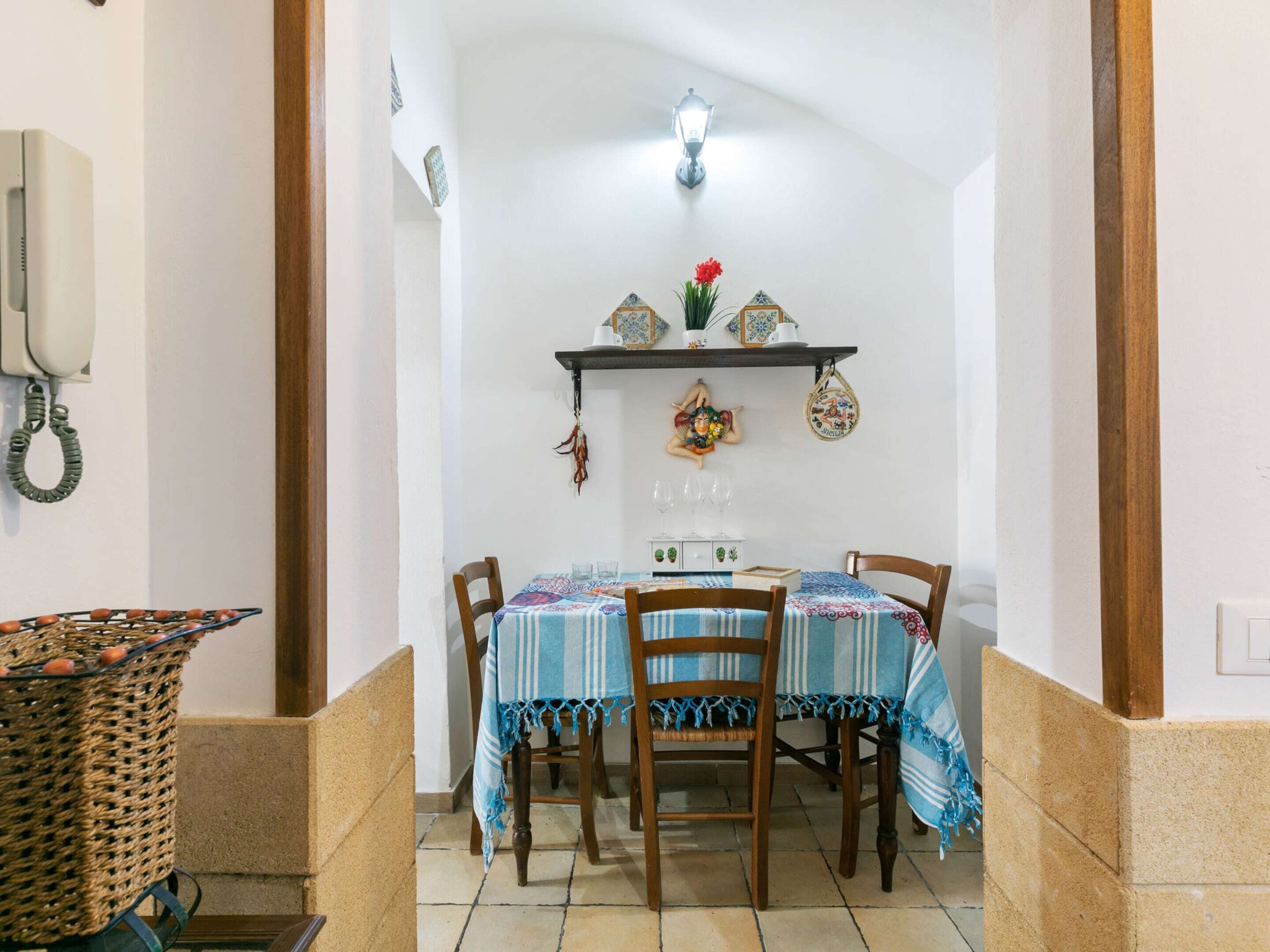 Un comedor con una mesa preparada para cuatro, una lámpara colgante y un teléfono instalado en la pared.