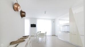 A modern kitchen with white cabinets, a dining area with a table and chairs, and a large window with sheer curtains. - Rivazzurra Homes - 57 (Termoli)