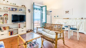 A spacious living area with a television, bookshelves, a wicker sofa, and a glass coffee table. - Holiday Home in Santa Tecla Near Etna Beach (Acireale)