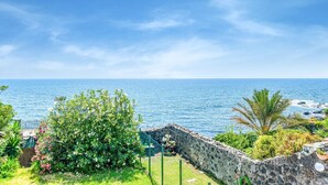 A coastal view with a stone wall, greenery, and a clear blue sky. - Holiday Home in Santa Tecla Near Etna Beach (Acireale)